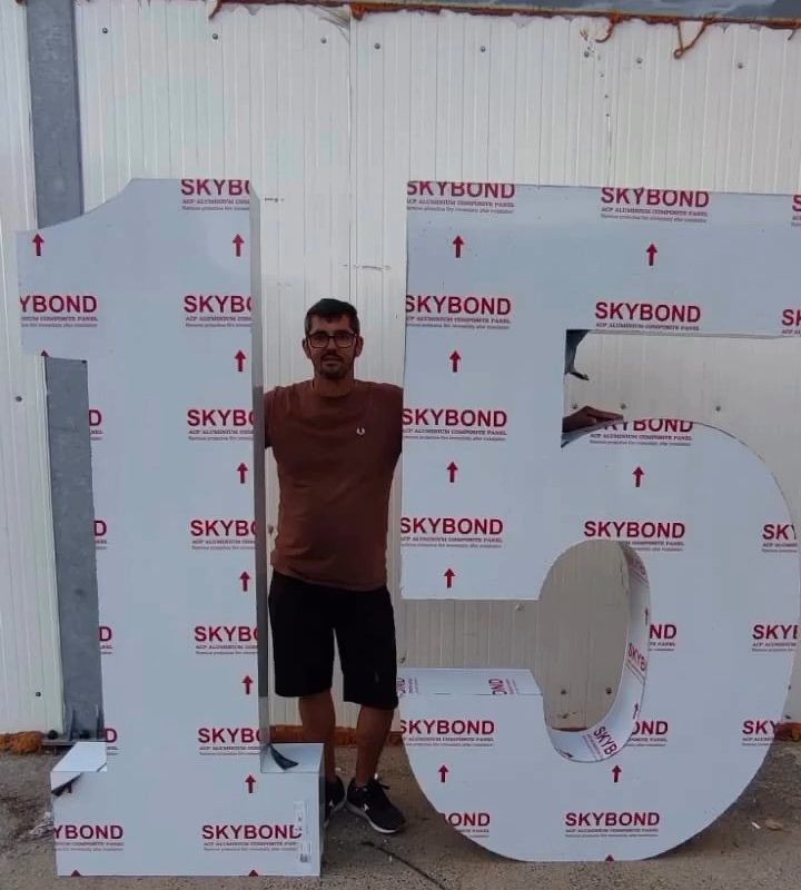 Números «15» gigantes em Dibond, ainda com a película de proteção, com uma pessoa ao lado para dar a escala